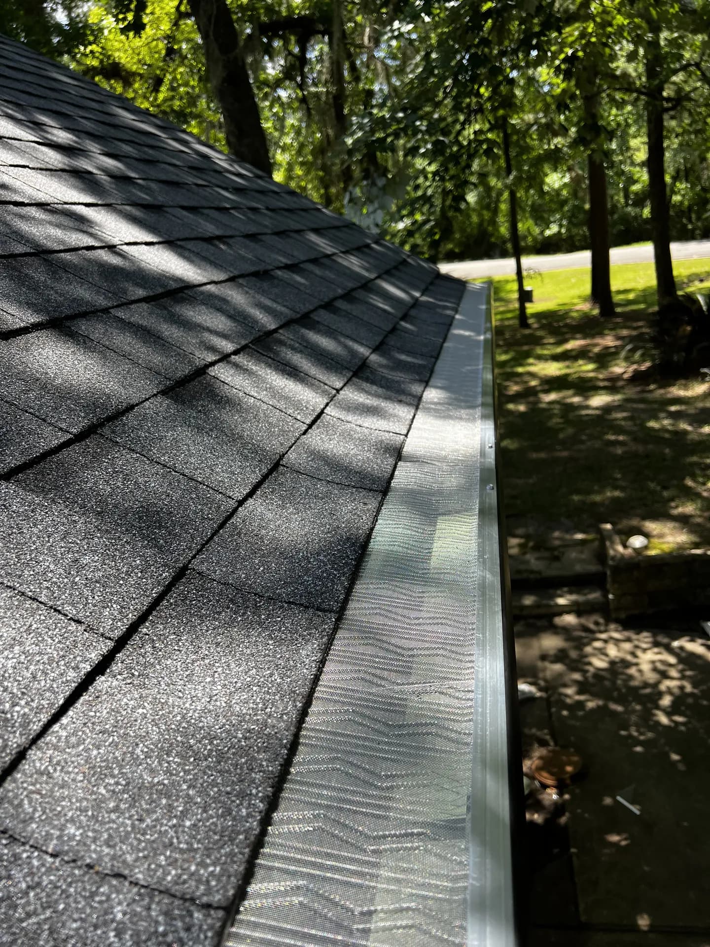Close-up of a newly installed gutter with mesh guard along a shingle roof eave