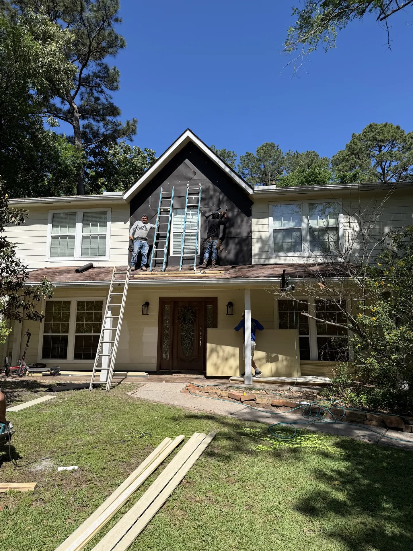 ROYH Build Co crew installing new siding on the gable of a home, carrying materials across the yard